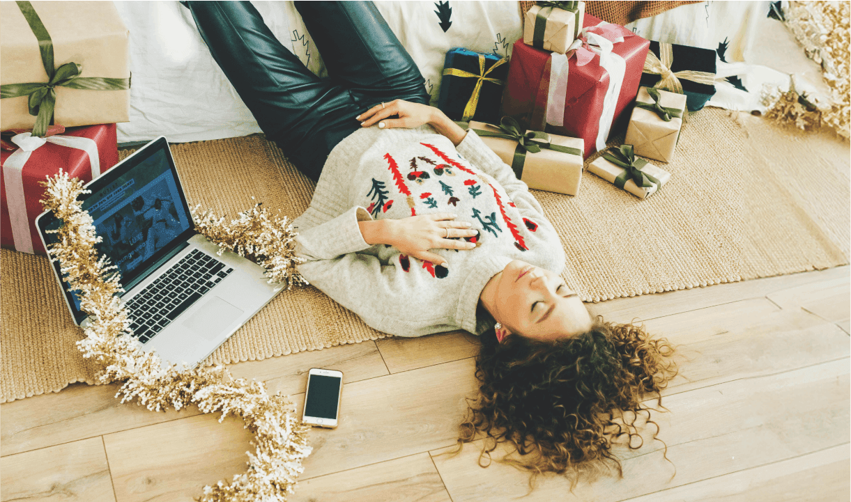 girl chilling on the floor of her appartment around christmas gifts and her laptop